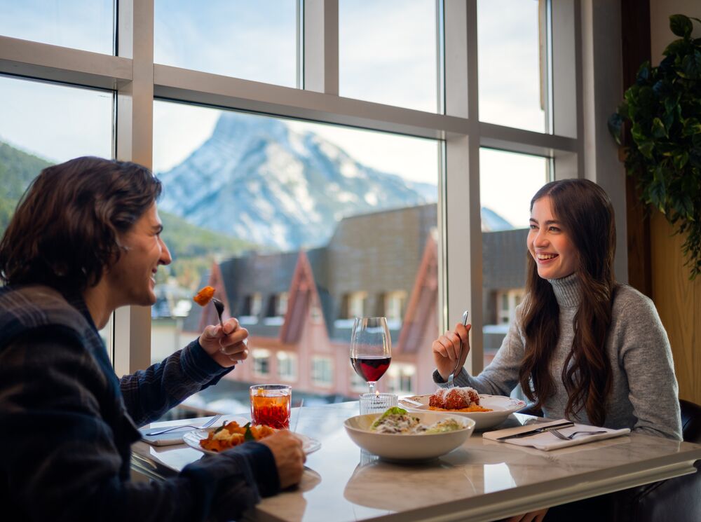A couple dines at Lupo in Banff National Park with Mount Rundle out the window in the background.